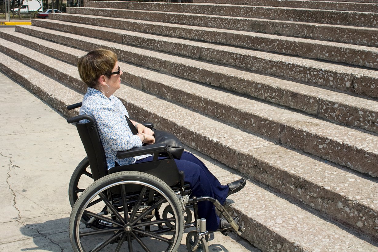 Lady sitting in a wheelchair at the base of stairs.